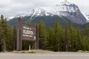 Willkommen in Alberta-Schild mit Kiefern und schneebedeckten Gipfeln der Rocky Mountains.