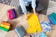 Top view a young woman in casual clothes stacks things, sorting them by colors and folding them into a metal mesh basket. Concept of smart tidy and cleanliness in the house