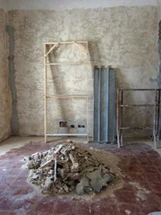 The dining room is completely empty with stripped walls and a pile of concrete in the center of the room, with unfinished tiling, as seen on HGTV's House Hunters International Renovation.