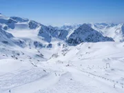Winterlandschaft mit schneebedeckten Berghängen und Pisten mit Skifahrern an einem sonnigen Frühlingstag im Skigebiet Stubai Gletscher, Stubaital, Tirol, Österreichische Alpen