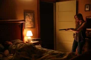 Cindy aiming a shotgun at sleeping Bob.