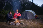 Checker Tobi (links) mit Bergführer Simon Gietl wärmen sich vor ihrem Zelt am Lagerfeuer.