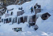 Arbeiter schaufeln riesige Schneeverwehungen von den Dächern von Eigentumswohnungen, während ein Schneepflug von Schneeverwehungen in den Schatten gestellt wird, wenn er den Parkplatz in Mammoth Lakes räumt, nachdem ein Blizzard im bisher größten Sturmsystem dieser Saison am Mittwoch bis zu 10 Fuß Schnee fallen ließ. 6. Februar 2019. Mammoth Mountain war am Dienstag wegen des Schneesturms geschlossen, wurde aber am Mittwoch wiedereröffnet.