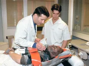 Dr. Roland Heilmann (Thomas Rühmann, li.) und Pfleger Vladi (Stephen Dürrüre.) kümmern sich um den Schwerverletzten.