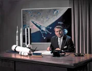 VON BRAUN, WERNHER-DR. IN HIS OFFICE WITH PHOTO OF MOON LANDER IN BACKGROUND AND ROCKET MODELS ON HIS DESK. 5/18/64 (MIX FILE)