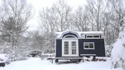 Snow flurries gently fall to the ground and cover Jesse and Nora's completed tiny house and traveling theater, on a blustery winter day, in Richmond, Rhode Island, as seen on Tiny House, Big Living