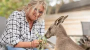 Theresa sitting down feeding a kangaroo.