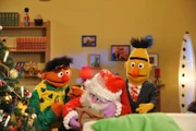 Ernie (li.) und Bert (re.) freuen sich riesig ĂĽber den Besuch des Weihnachtsmanns (Mi.).Â