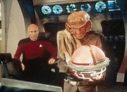 Bei einem Zusammentreffen zwischen der Enterprise und einem Ferengi-Schiff uebergibt dessen Commander Dai Mon Bok (Frank Corsentino) Captain Picard (Patrick Stewart) das Wrack der U.S.S. Stargazer, welches dieser neun Jahre zuvor bei der Schlacht von Maxia verloren hatte.