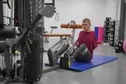Niklas ist im Trainingsraum und sitzt an einem Gerät, welches die Armmuskulatur trainiert. Er trainiert sehr fokussiert.