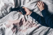 Cropped shot of woman lying on bed with gun in her hand