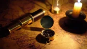 Kompass und Fernrohr auf alter Weltkarte im Kerzenlicht