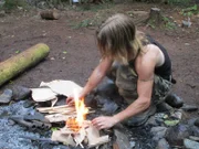 Bear Brown starting a fire with cardboard and kindling at the campsite.
