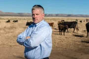 Ken Cage standing outside in a cow field with his arms crossed.