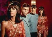 Dr. McCoy (DeForest Kelley, 2.v.l.) und Mr. Spock (Leonard Nimoy, 2.v.r.) beobachten leicht abgestoßen die fremde Welt von Harry Mudd. Der Herrscher hat sich eine Bevölkerung aus Androiden geschaffen, über die er verfügen kann. Die Roboter-Frauen (Darstellerinnen unbekannt) gleichen einander wie ein Ei dem anderen.
