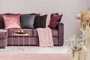 Kupfertisch vor einer violetten Couch mit dekorativen Kissen im eleganten Wohnzimmerinterieur