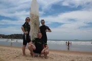 Entertainment-Managerin Cori, zweiter Offizier Christian Baumann und Mitglied des Showensembles Esther posieren mit Surfbrett in Buzios, Brasilien.