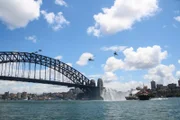 Hubschrauber, Schleppboote und die Sydney Harbor Bridge an einem sonnigen Tag.