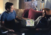 Mulder (David Duchovny, l.) besucht die hochschwangere Scully (Gillian Anderson, r.), um ihr ein Geschenk zu überreichen.