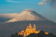 Die Vulkane prägen die Landschaft und Kultur in Mexiko. Die Iglesia de Nuestra Señora de los Remedios ist eine mexikanisch-katholische Kirche aus dem 16. Jahrhundert, die auf der Tlachihualtepetl-Pyramide in Cholula erbaut wurde. Im Hintergrund der mächtige Popocatépetl.