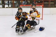 Beim Sledgehockey sitzen die Spieler in einem Schlitten mit Kufen darunter. Links: Checker Tobi.