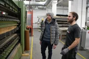 Ab dem Frühjahr werden die Base Ski in einer Produktionsstätte nahe Salzburg hergestellt. Vor Ort informiert sich Jasper (l.) über letzte Details. Ein Mitarbeiter erklärt ihm die verwendeten Maschinen.