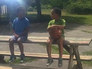 Two children talking on a picnic table.