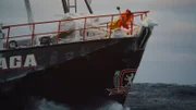 Deckhands breaking ice at the bow of the icy F/V Saga at sea.