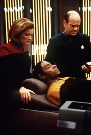 Der Doktor (Robert Picardo, r.) und Captain Janeway (Kate Mulgrew, l.) sind besorgt um Tuvok (Tim Russ, liegend), der nach einem Angriff fremder Wesen ins Koma gefallen ist.