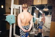 Justin (Jarno Mindner) post vor einem Spiegel auf der Trainingsfläche. Genau dann, als Mia Felix durch das Studio führt.