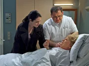 Dr. Elena Eichhorn (Cheryl Shepard, links) ist gerade auf dem Weg zum Ärzteball, als Hans-Peter Brenner (Michael Trischan) sie in das Zimmer von Ilse Friedel (Ingeborg Krabbe, liegend) ruft. Ilse Friedel, die Elena am Oberschenkel operiert hat, hat plötzlich starke Schmerzen im Bauch.