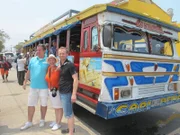 Passagiere Isabell und Bastian mit Reiseleiter Thorsten vor einem bunten Bus, in dem die "Rumba en chiva" stattfindet, eine "feucht-fröhliche Party-Stadtrundfahrt" durch Cartagena
