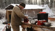 Tyler preparing meat on the table outside his wood cabin.
