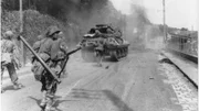 Amerikanische Truppen bewegen sich auf dem Weg nach Paris in Richtung Fontainebleau, während der Rauch von gesprengten deutschen Panzern den Himmel erfüllt.