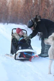 Ashley and Sydney Selden in the dogsled; Tyler Selden bent over talking to them.