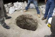 San Diego, CA: Four men looking into an underground tunnel. Tunnels like this are used by smugglers to traffic their contraband across the border.