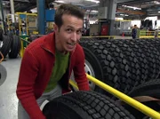 Willi schaut in der Autofabrik zu, wie aus vielen Einzelteilen Schritt für Schritt ein großer Laster entsteht. Er versucht, ein LKW-Rad zu heben.