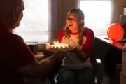 Eine glückliche Frau sieht einen Mann an, der ihr einen Geburtstagskuchen bringt