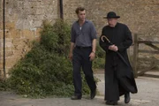 Sid (Alex Price, l.) und Father Brown (Mark Williams, r.) wandern einen Feldweg entlang.