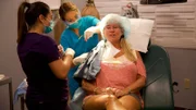 Cheri sits up as Dr. Lee, with the help of Val, performs surgery on her.