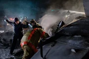A rescuer (played by a background actor) calls for help as a firefighter (played by background actor) peers inside the wreckage of Continental Airlines Flight 1713.