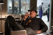 "Nachtschicht - Reise in den Tod": Clemente (Christian Redl) sitzt rauchend und mit Füßen auf dem Tisch an seinem Schreibtisch.