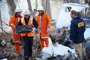 Investigator Bob Benzon (played by Kevin Carter) looks on as recovery workers (played by background actors) carry the black boxes of Alitalia flight 404.