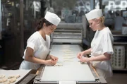 Alexandra (Julia Richter, re.) und Paula (Mariam Hage) am Fließband der Großbäckerei und scherzen über ein besseres Leben.  - Foto aus Folge 1 -