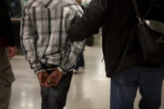 Jamaica, New York, USA: HSI agents escort a passenger in handcuffs after they discover heroin in his suitcase. (Photo Credit: National Geographic Television)