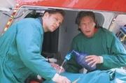 Thomas Wächter (Manfred Stücklschwaiger, li.) und Dr. Lüdwitz (Rainer Grenkowitz) bringen den schwerverletzten Terroristen Tomasz (Andre Andruza) in den Helicopter.