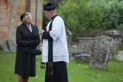 Mrs McCarthy (Sorcha Cusack, l.) berichtet Father Brown (Mark Williams, r.), dass sie dem Witwer Sir Aaron Armstrong ihre Hilfe angeboten hat.