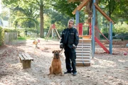 Paul Dänning (Jens Münchow) sammelt auf dem Spielplatz einen streunenden Wachhund auf und legt ihm einen Maulkorb an.