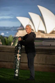 Portrait of Jeremy Wade standing with rod case, with Sydney Opera House in the background.