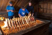 Finland - L to R: Marku and Kimmo teach Gordon Ramsay the traditional way to cook whitefish. After resting for 24 hours, the fish are roasted on sticks over an open fire. (Credit: National Geographic/Justin Mandel)